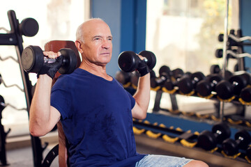 A portrait of senior man in the gym training with dumbbells. People, health and lifestyle concept