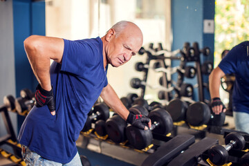 A portrait of senior man feeling strong back pain during training in the gym. People, healthcare and lifestyle concept