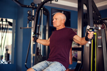 Fototapeta na wymiar A portrait of senior man in the gym training chest muscles. People, health and lifestyle concept