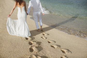 Fototapeta na wymiar The bride and groom walk hand in the sand. footprints in the sand near the ocean
