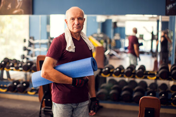 A portrait of senior man keeping yoga mat and looking at camera. People, healthcare and lifestyle concept