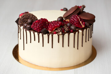 cake with white cream, chocolate drips, pomegranate, nuts and chocolate decor