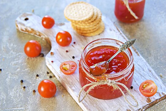 Tomato jam in a glass jar on a light concrete background. Jam recipes.