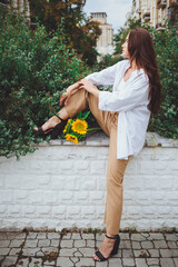 Young happy beautiful girl is walking in a shirt and pants with a bouquet of flowers of sunflowers on a city street