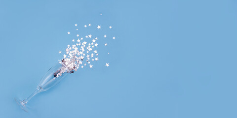 Glass of champagne and silver starry confetti on blue background. Celebrating birthday and new year. Festive banner