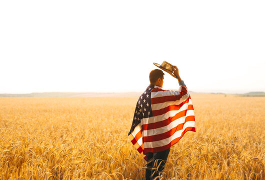 Young caucasian farmer energetically raised the US flag in a picturesque field of wheat.