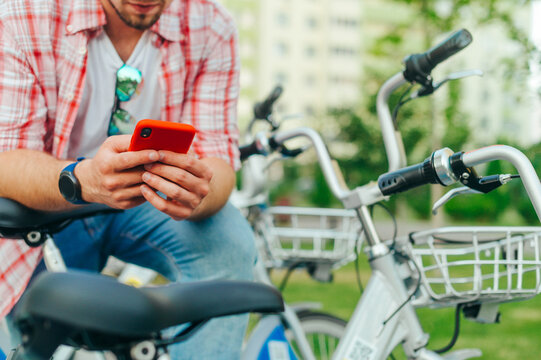 Man with a bicycle uses a smartphone. Close-up photo of men's hands using a mobile application for sharing bicycles. Background