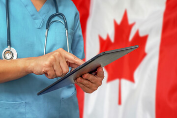 Surgeon or doctor using a digital tablet on the background of the Canada flag. Medical equipment or...