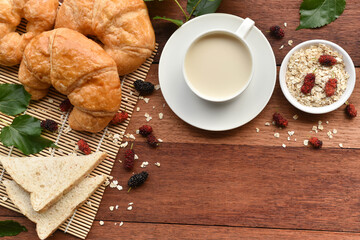 Milk along with croissants and bread on wooden table in breakfast concept.