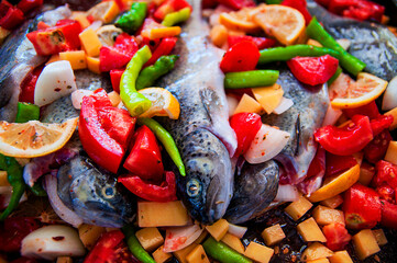 Baked trout with tomatoes, green peppers, lemon, onion and potatoes on a baking tray.