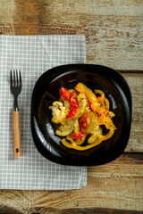Vegetable stew on a black plate on a wooden table.Copy place.
