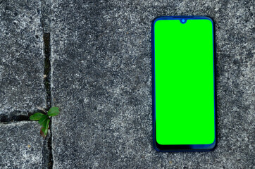 Smartphone placed on a white and black stone floor. Special green screen for inlay on the phone,