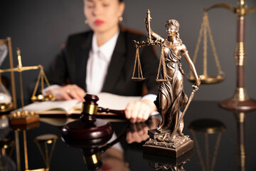 Young female lawyer during work in chamber. Gavel , Themis statue and scale on the brown shining desk.