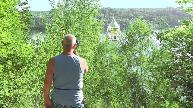 A male blogger with a mobile phone about travel talks about the temple from the back.