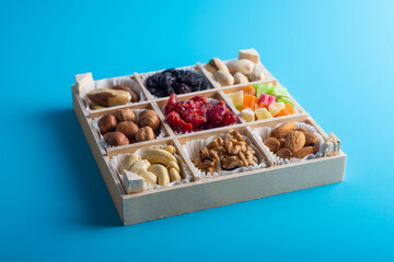 Assorted dried fruits and nuts in a wooden box isolated on a blue background. Raisins, candied fruits, cherries, Brazil nuts, hazelnuts, walnuts, almonds, cashews, pistachios.