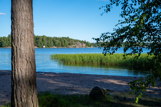 Swimming beach in the shade during a sunny summer day with a wooden island in the background.