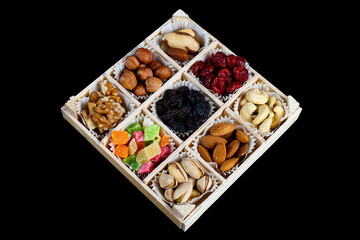 Assorted dried fruits and nuts in a wooden box isolated on a black background. Raisins, candied fruits, cherries, Brazil nuts, hazelnuts, walnuts, almonds, cashews, pistachios.