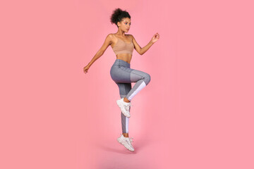 Sporty woman practicing squat exercises in studio. African woman in sportswear working out on pink background. - obrazy, fototapety, plakaty