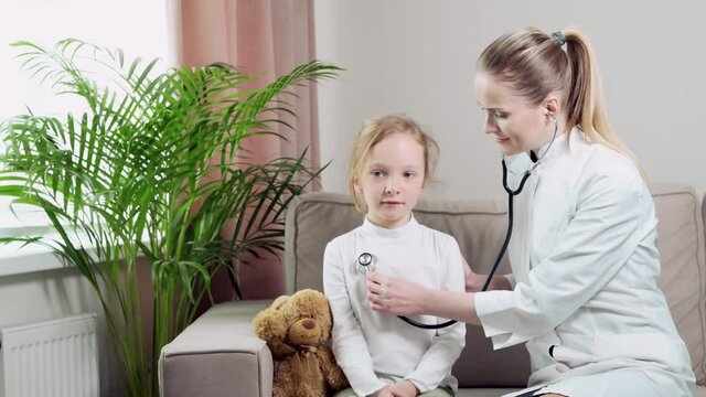 A female doctor in white medical coat is listening to child with a phonendoscope