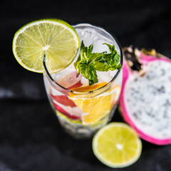 Refreshing cocktail with lime, mint, ice, grapes and orange on a black background with lime and dragonfruit