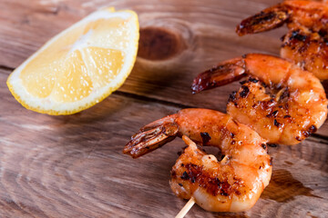 Appetizing fried shrimp on a skewer on a wooden surface among lemon and seasonings. The concept of fast and wholesome food