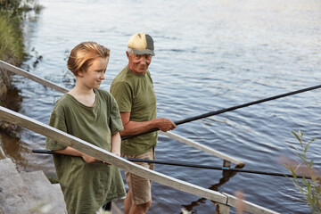 Father and son fishing on wooden stairs leading to water,, grandfather teaching his grandson to catching fish, family spending weekend together near lake.