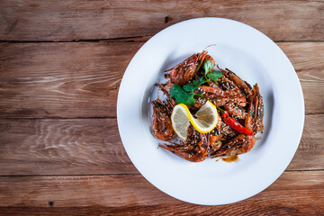 Appetizing fried shrimp with specialties, sesame seeds and lemon, on a white plate on a background of wood. Food concept in restaurants and bars