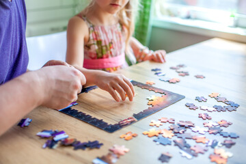Father and daughter assemble the puzzle while sitting at the table. Games during rain and bad weather, quarantine. Family relaxing educational games at home.