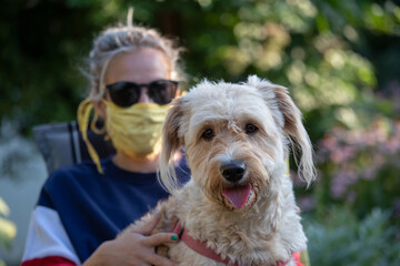Girl with mask holding dog in lap in garden