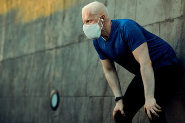 Exhausted athletic albino man with face mask taking a break after jogging outdoors.