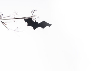 Bat of paper flaying under a brunch on a white background. Homemande Halloween decoration, DIY. Creative trendy minnimal Halloween concept for card or poster with copy space