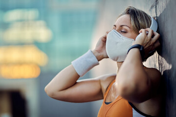 Athletic woman with protective face mask listening music with eyes closed outdoors.