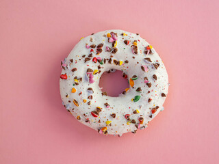 Homemade circle donut with white icing and choclate rainbow sprinkles on a trendy pink background situated in the center of image. Tasty doughnutdonut, top view. Sweet food leftlovers