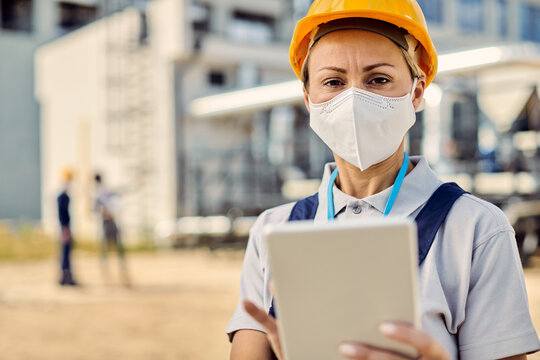 Female civil engineer wearing protective face mask while using touchpad at construction site.