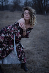 Fototapeta premium Young beautiful girl in a dark dress against the background of the field, curly hair