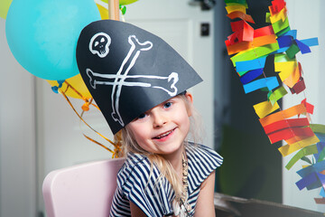 A cheerful little child in a pirate costume plays at home on a cardboard sea ship with a black...