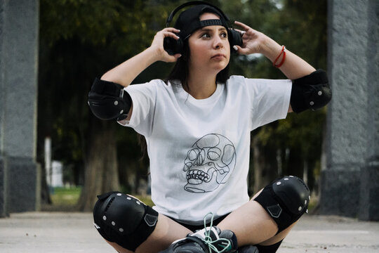 Joven mujer skater est&aacute; en el suelo acomodando sus aud&iacute;fonos