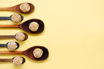 Healthy organic energy balls with nuts and honey in coconut. vegan vegetarian raw snack or sports snack food in wooden spoons on a yellow background.