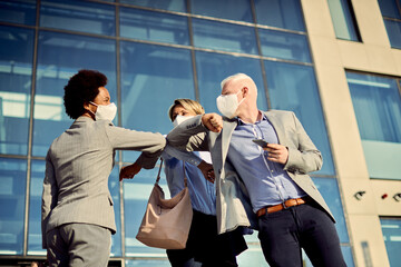 Obraz premium Happy business colleagues with face masks elbow bumping while greeting outdoors.