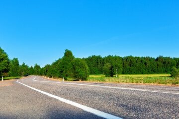 Country asphalt road, green fields and forest at summer
