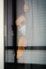  Quarantine man in medical mask on face  looking through the window.