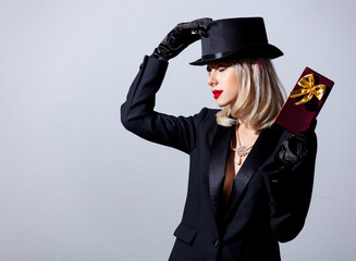 Blonde woman in black jacket and top hat with gift box on white background