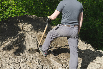 A man standing with a shovel near a hip of soil. Relaxing.