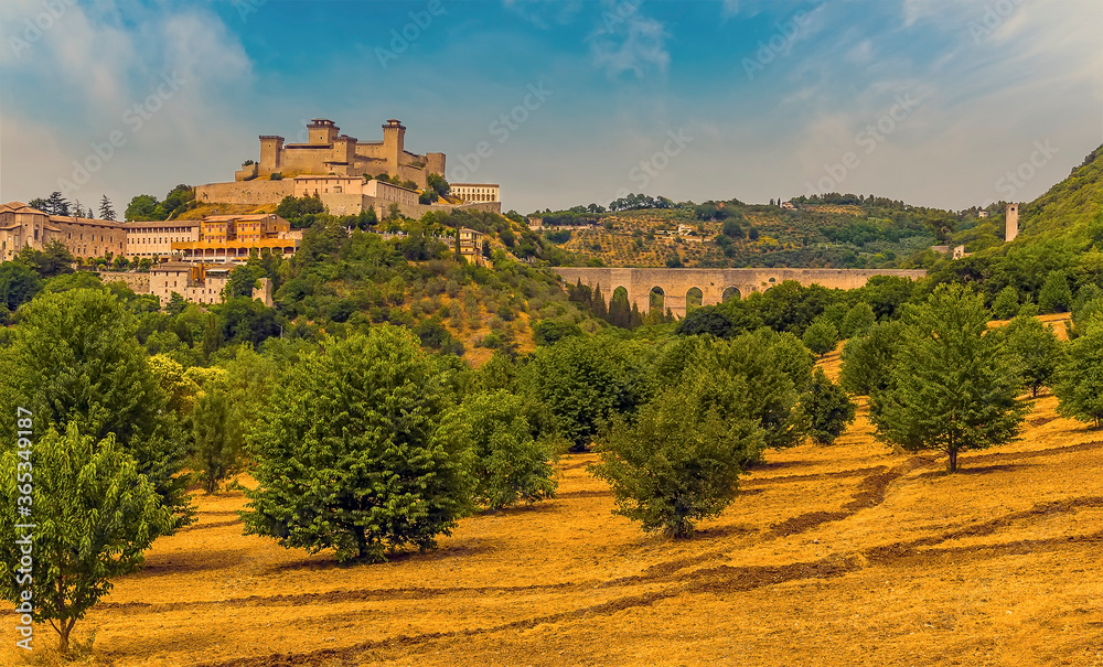 Wall mural A view across a straw lined olive grove towards the Tower Bridge and the hill top fortress in Spoleto, Italy in summer