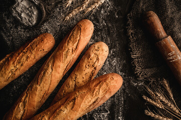 Freshly bread baguettes on black slate background with wheat spikelets, sackcloth, rolling pin. Pastries and bread in a bakery, Food concept, top view