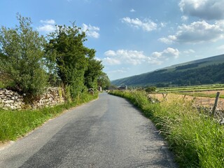 Fototapeta na wymiar Country road, leading to Kettlewell, with dry stone walls, trees, grasses, and fields near, Buckden, Skipton, UK 