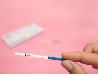 Female hand holding positive pregnancy test isolated on pink background. The abbreviation HCG on the blue bar means Human chorionic gonadotropin is a hormone produced by cells that are surrounding a