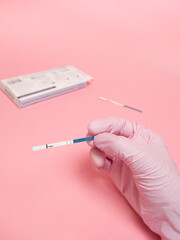 Female hand in a pink medical glove holding positive pregnancy test isolated on pink background. The abbreviation HCG on the blue bar means Human chorionic gonadotropin is a hormone produced by cells
