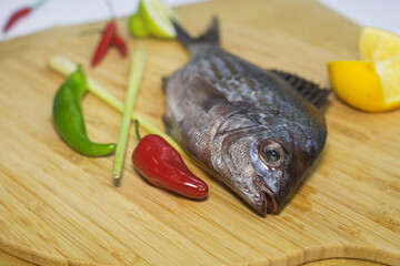 fresh fish of silver color is lying on a wooden Board next to a hot pepper