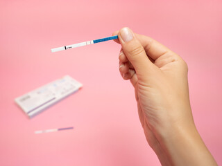 Female hand holding positive pregnancy test isolated on pink background. The abbreviation HCG on the blue bar means Human chorionic gonadotropin is a hormone produced by cells that are surrounding a